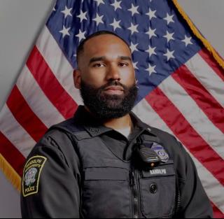portrait of Officer Vincent Burton, Randolph Police Department, in uniform with an American flag in the background.
