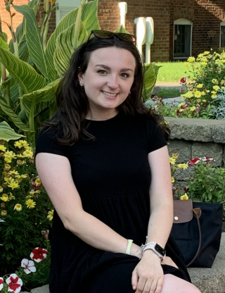 photo of Samantha Bradley sitting on a stone wall in front of various plants