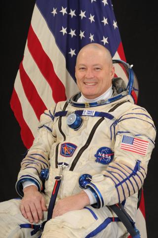 portrait of Commander Scott Tingle in an astronaut's suit, sitting in front of an American flag.
