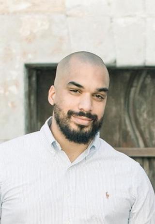 Portrait of Joao Barbosa in white dress shirt, standing in front of a stone building.