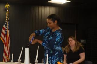 photo of Isabel Davila-Lynch lighting a candle in front of Michelle Barley